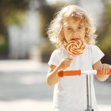 Petite fille à trottinette qui mange une sucette sucrée.