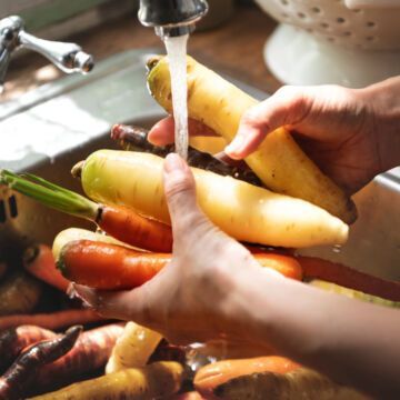 Personne qui lave des légumes dans son évier en faisant attention à bien les laver.